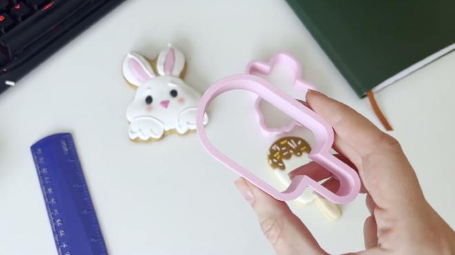 Finished pink custom cookie cutter with decorated cookies on a desk