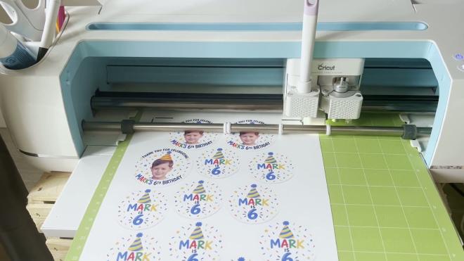 Cricut cutting a sheet of Mark is 6 birthday stickers on a green cutting mat
