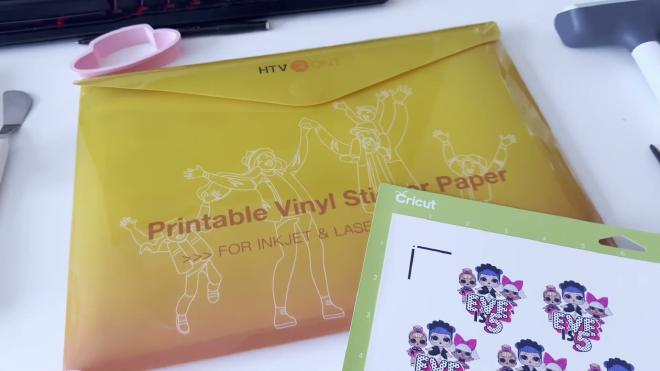 HTVRONT printable vinyl sticker paper package next to a printed Eve is 5 sticker sheet on a Cricut mat